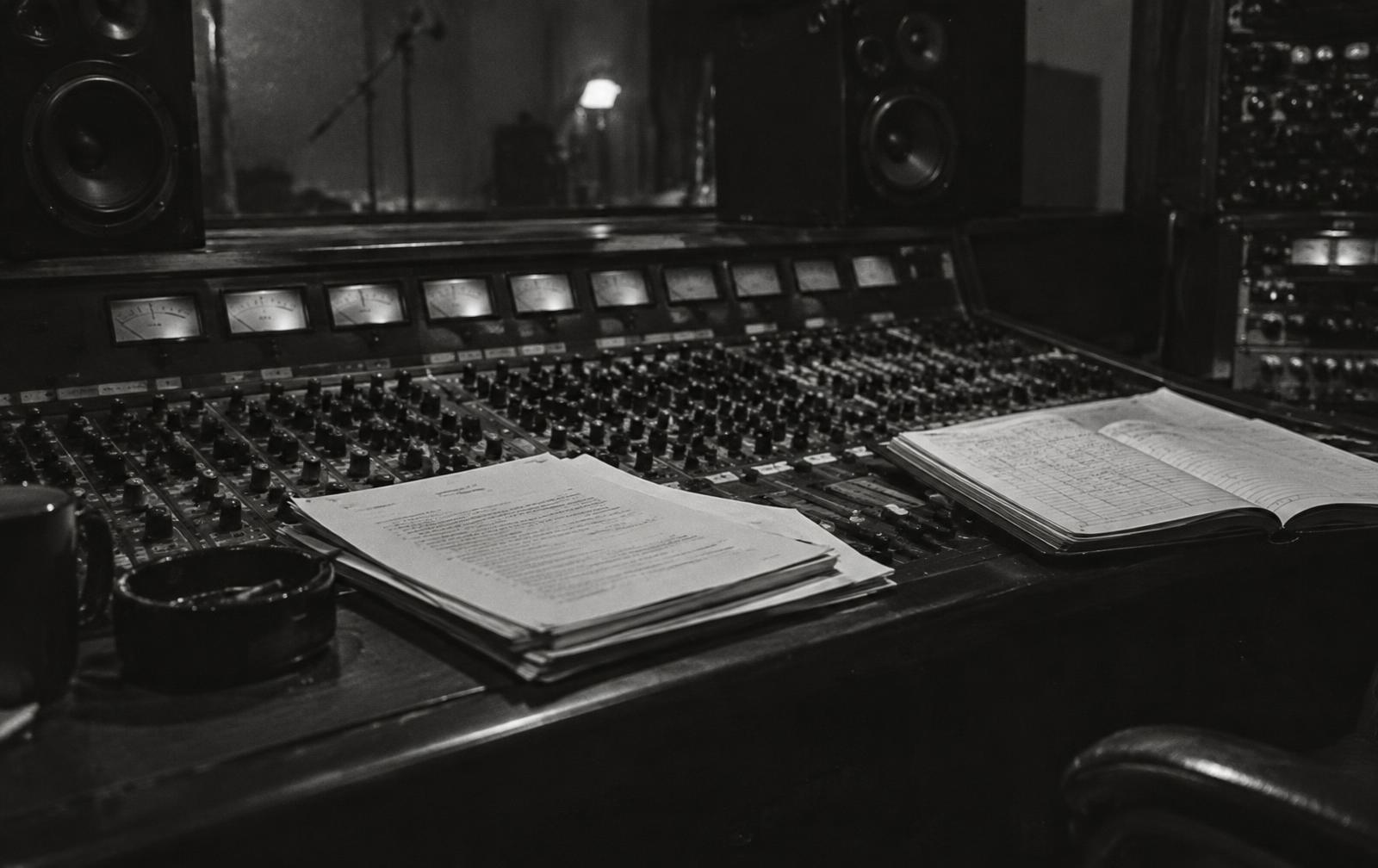 Archival-style still of a studio mixing console with contracts and a ledger